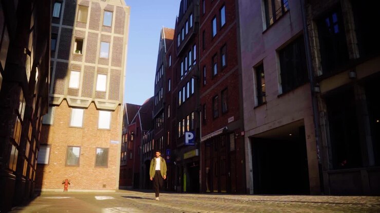 Vista a livello strada che mostra un giovane uomo che cammina per le vie storiche vicino a Grote Markt ad Anversa con edifici in mattoni, viuzze e calda luce diurna. Tranquilla scena di esplorazione urbana in una città europea