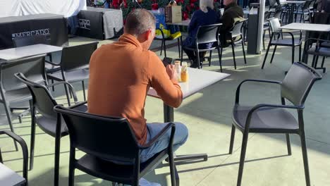 un hombre usando su teléfono celular y tomando café y jugo de frutas en un café callejero en cascais en un día soleado