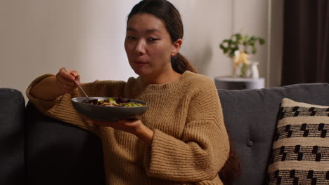 집에서 소파에 앉아 건강한 채식주의자 또는 채식주의자를 먹고 씨과 함께 러드 잎을 먹고 와인 한 잔을 입고 노트북 1에서 쇼를보고 있습니다.
