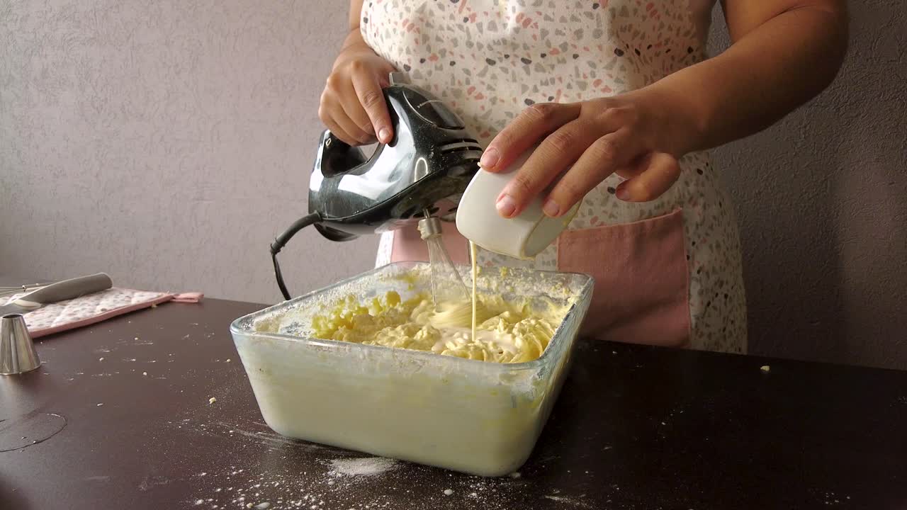 Donna latina con un grembiule che prepara un dolce versando il latte nell'impasto e usando lo sbattitore