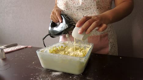 Lateinische-Frau,-Die-Eine-Schürze-Trägt,-Bereitet-Das-Kochen-Vor,-Backt-Einen-Kuchen,-Gießt-Milch-In-Den-Teig-Und-Benutzt-Den-Mixer