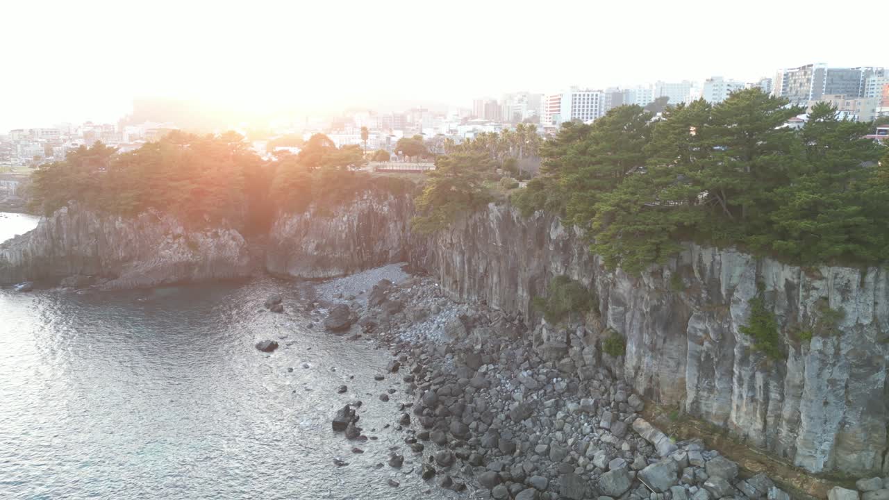 Drone aerial view in South Korea near a cliff with green trees over rocky area sunset light jeju island