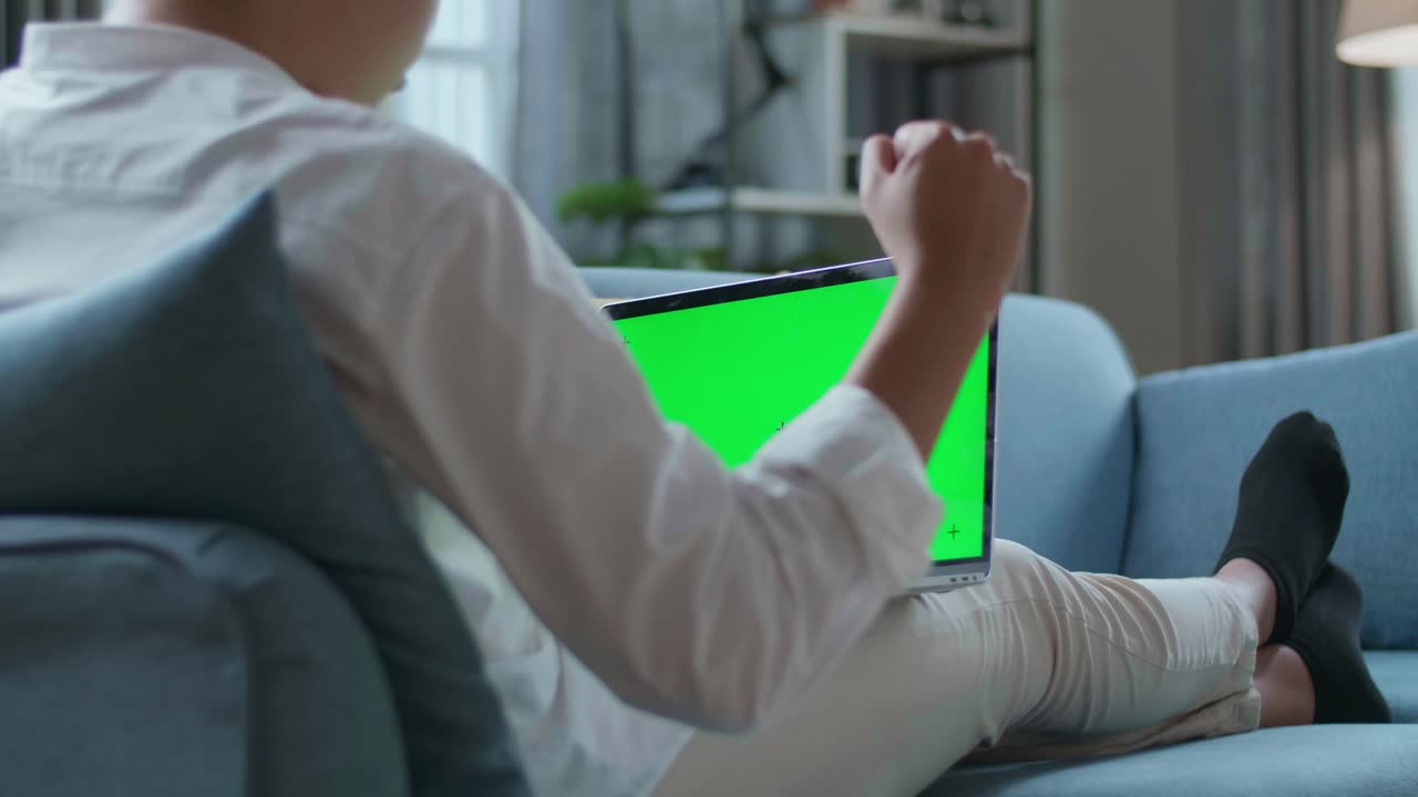 Man Celebrating While Lying On Sofa And Using Green Screen Laptop In The Living Room