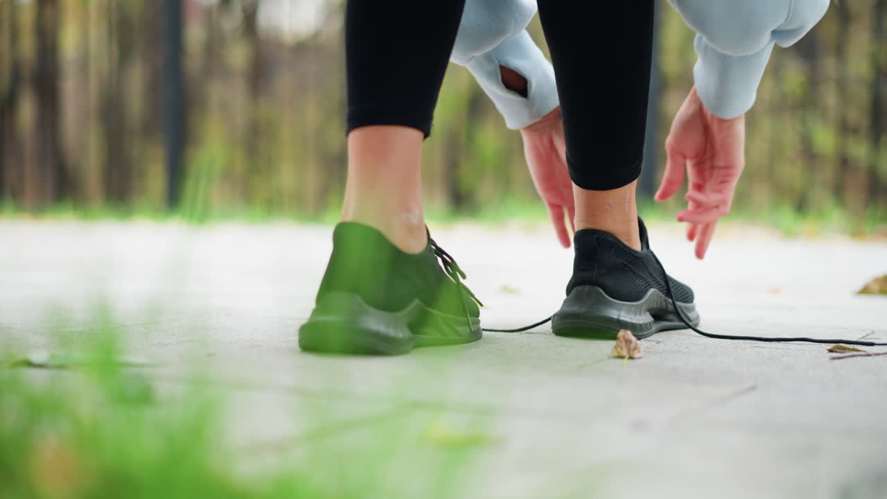 Close-up view of girl in black leggings adjusting her shoe lace, she is preparing for an outdoor run or workout, focusing on fitness and athletic preparation in a park