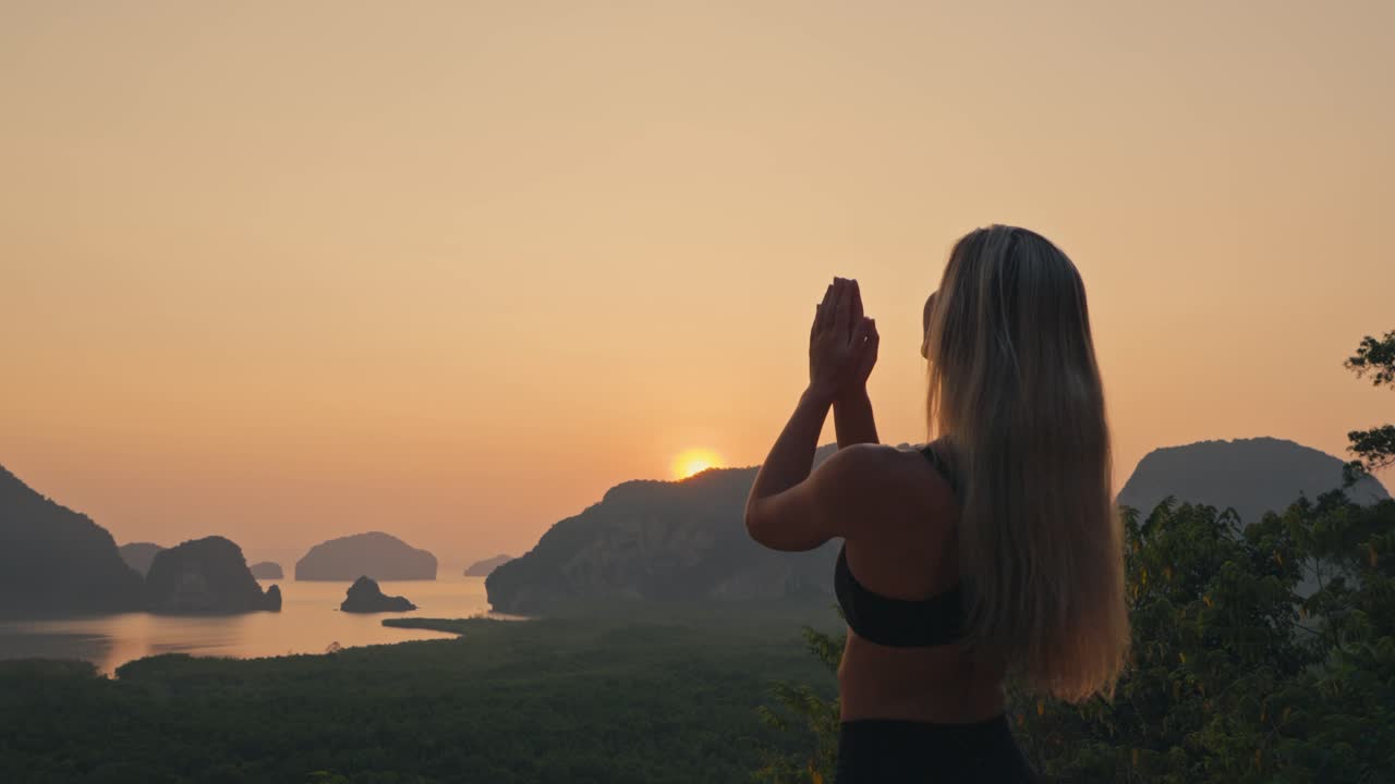Mujer rubia en postura de oración, levanta los brazos al cielo y regresa las manos al corazón. Movimiento de yoga calmado y consciente que expresa equilibrio, gratitud y bienestar.