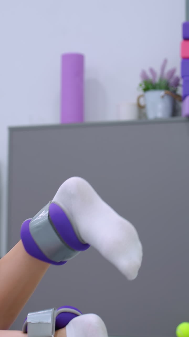 vista parcial de una mujer ejercitando los músculos de las piernas levantando la pierna con un pequeño peso unido, contra un telón de fondo de gimnasio con equipos