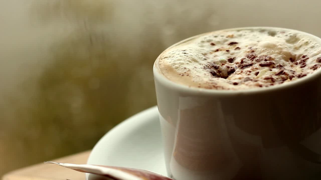 Cappuccino caldo fumante con schiuma e scaglie di cioccolato.