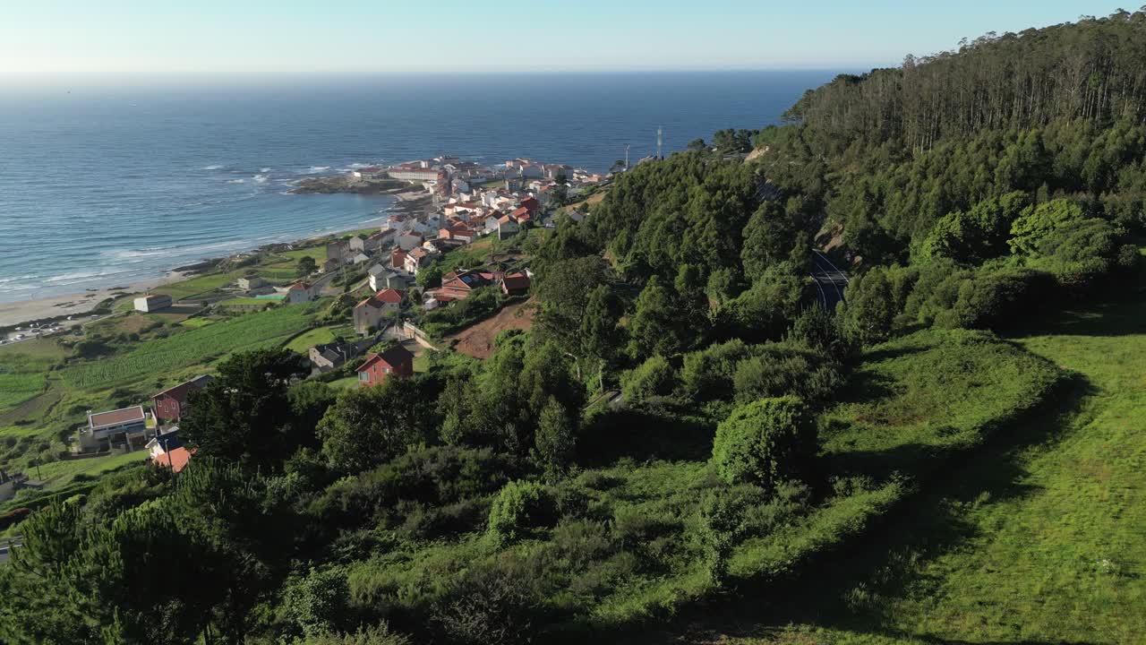 Flyvende over bjergsideby ved kysten med grønt landskab på en solrig morgen