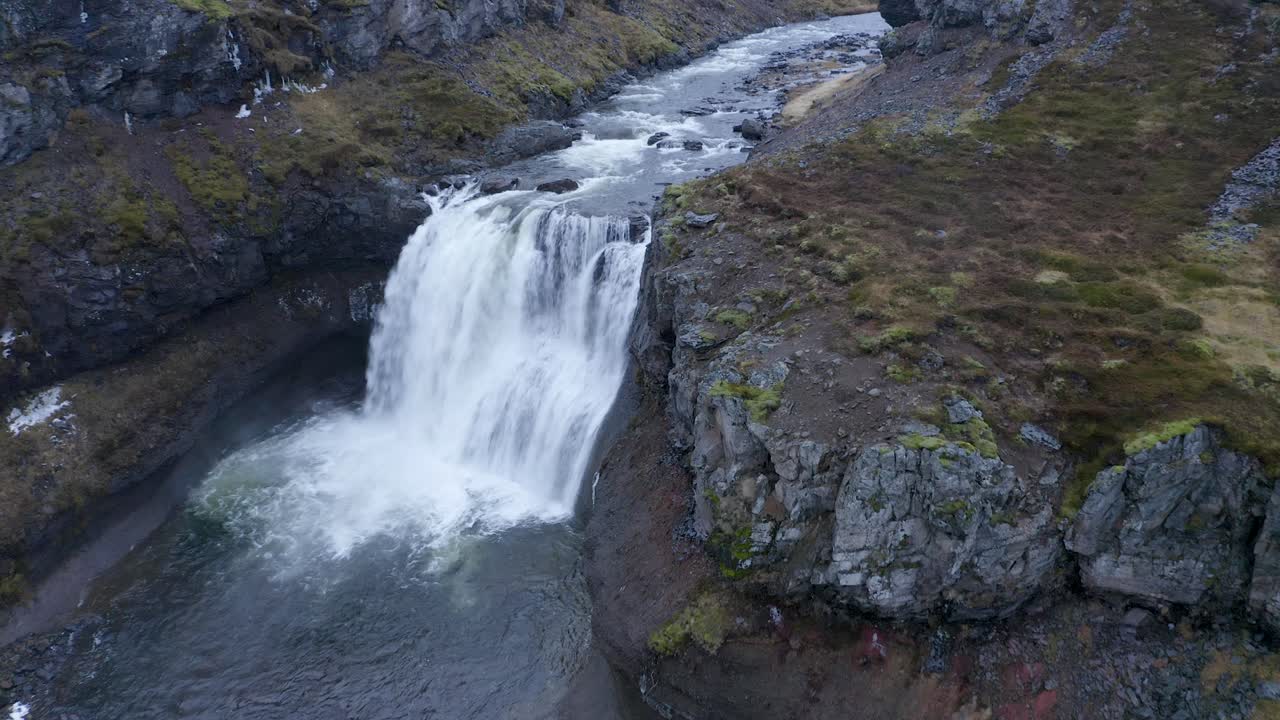 toma aérea descendente del agua que se estrella de la cascada en el río sela - islandia, europa