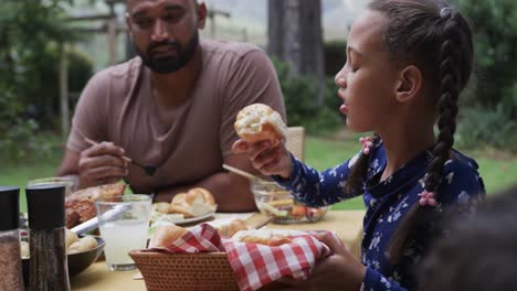 happy biracial father and daughter eating meal at dinner table in garden, slow motion