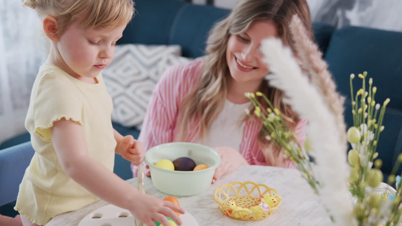 Young girl paints Easter egg with mother watching. Child focused, mother smiling warmly. Bright, cheerful home scene. Perfect for holiday, family, or craft-themed projects