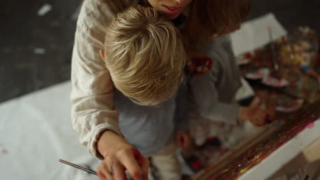 creative female painter creating artwork with children on easel in art studio.