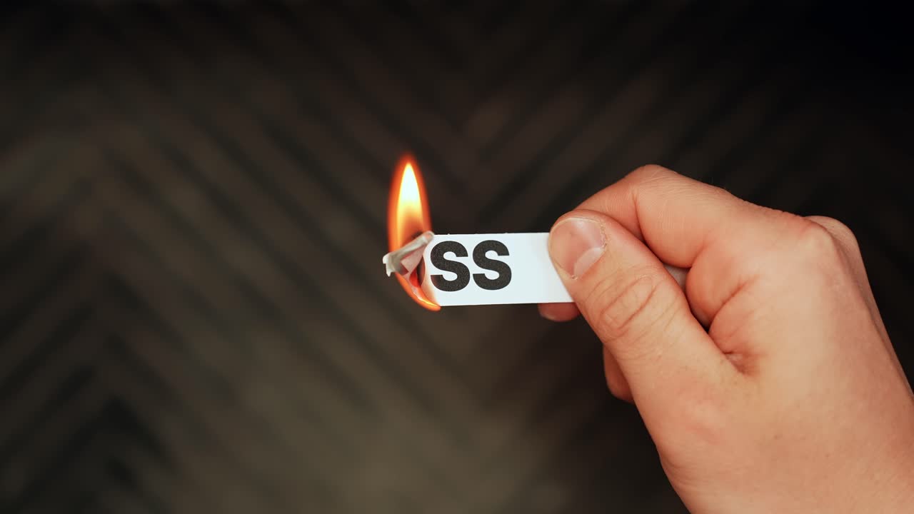 Hand burns a paper label reading “LOSS” against a dark background, symbolizing grief or financial setback. Strong copy space for dramatic concepts and ads
