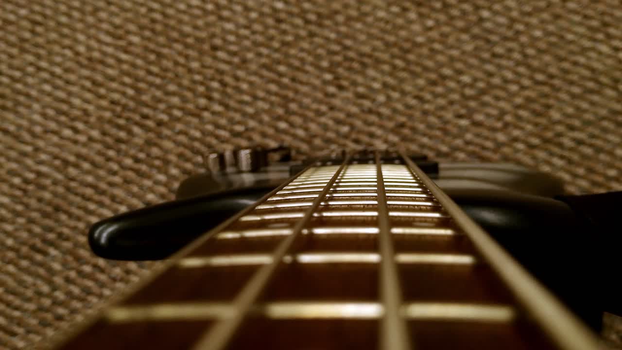 Dolly out of black bass guitar neck sliding over strings, close up