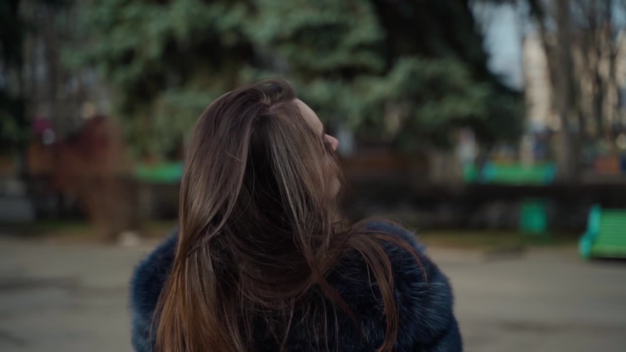Pretty girl with hot drink outdoors. Attractive young woman in luxury fur coat enjoys coffee in the city park. Slow motion.
