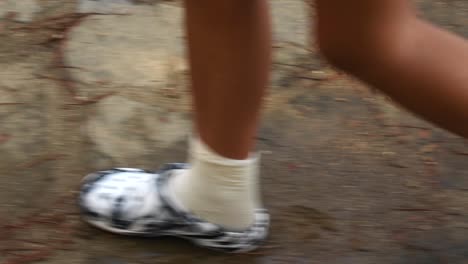 side view of woman legs in white flip flops walking in wet floor in the forest