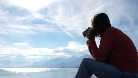 cinematic video of a person drinking coffee whilst looking out over the sea and enjoying her headspace on a chill summers day by the water