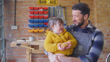 Father-With-Down-Syndrome-Daughter-Eating-Cake-In-Home-Workshop