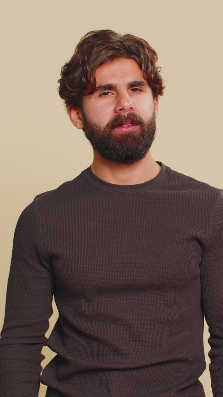 Frightened young man closing mouth with hands refusing to tell terrible secret on beige background