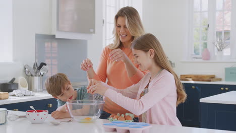 mother with two children in kitchen at home having fun baking cakes together