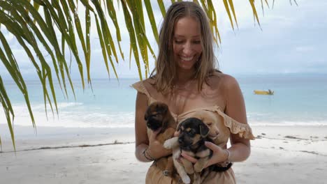 ultra slow motion shot of happy caucasian woman holding three puppies on tropical beach at asu island, north sumatra, indonesia