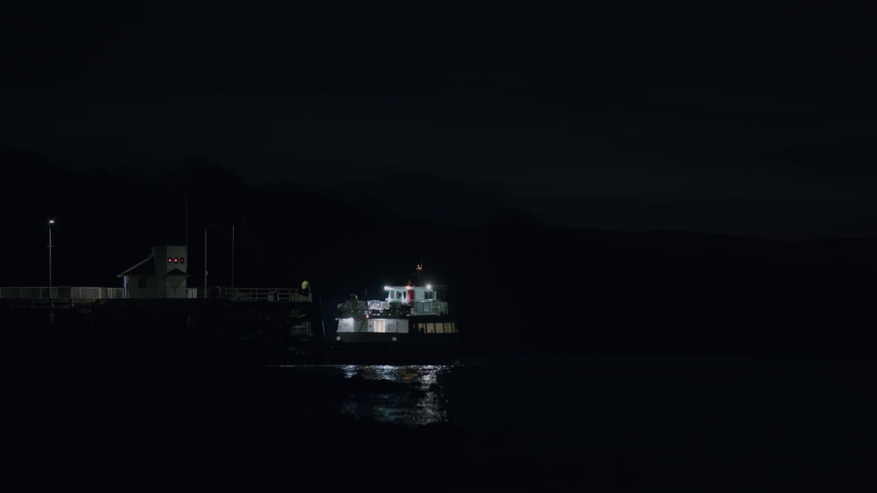 Ferry boat driving away from pier at night, distant static shot