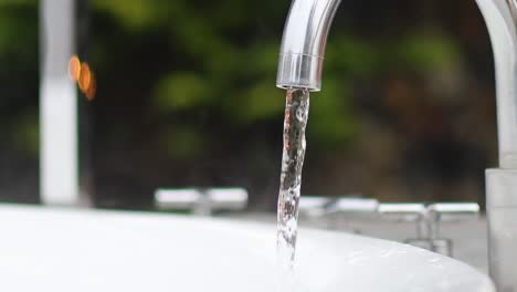 a detailed view of water streaming steadily from a shiny metal faucet into a white basin.