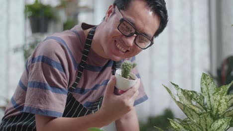 close up of smiling asian man looking at cactus plant in hand and shaking his head