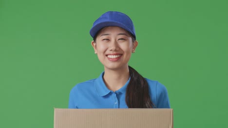 close up of asian female courier in blue uniform smiling while delivering a carton on green screen background in the studio