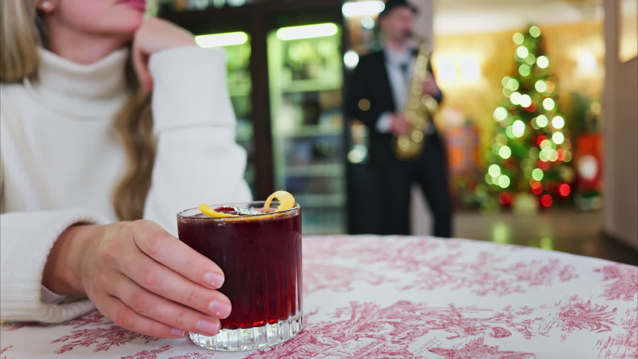 Close up of a woman holding a negroni cocktail on a red and white tablecloth at a restaurant with a Christmas tree on the background