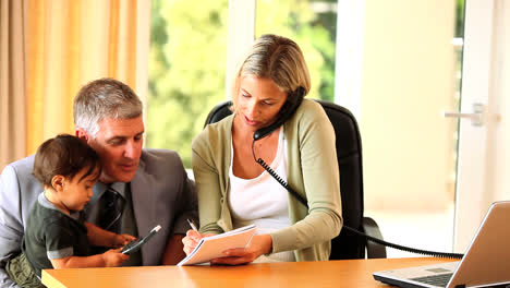 Young-woman-doing-office-work-while-husband-holds-baby