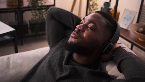 man listening music on headphones while leaning on sofa