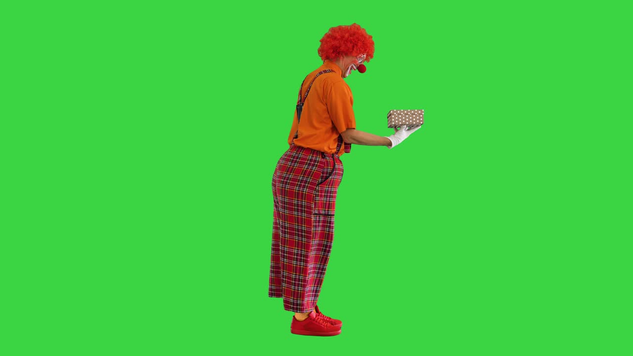 Happy clown holding a box with a gift on a Green Screen, Chroma Key