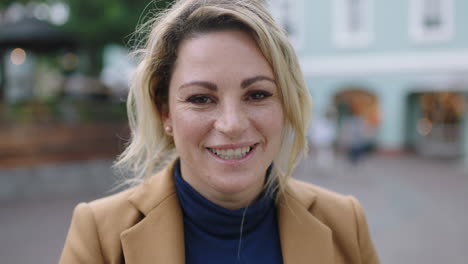 Retrato-En-Cámara-Lenta-De-Una-Elegante-Mujer-De-Negocios-Rubia-Con-Traje-Sonriendo-Alegre-En-El-Fondo-Urbano-De-La-Cámara