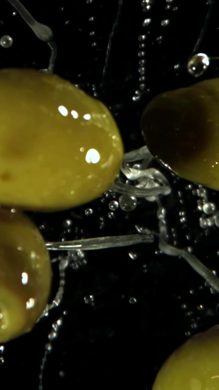 Primo piano di olive verdi con schizzi d'acqua su sfondo nero