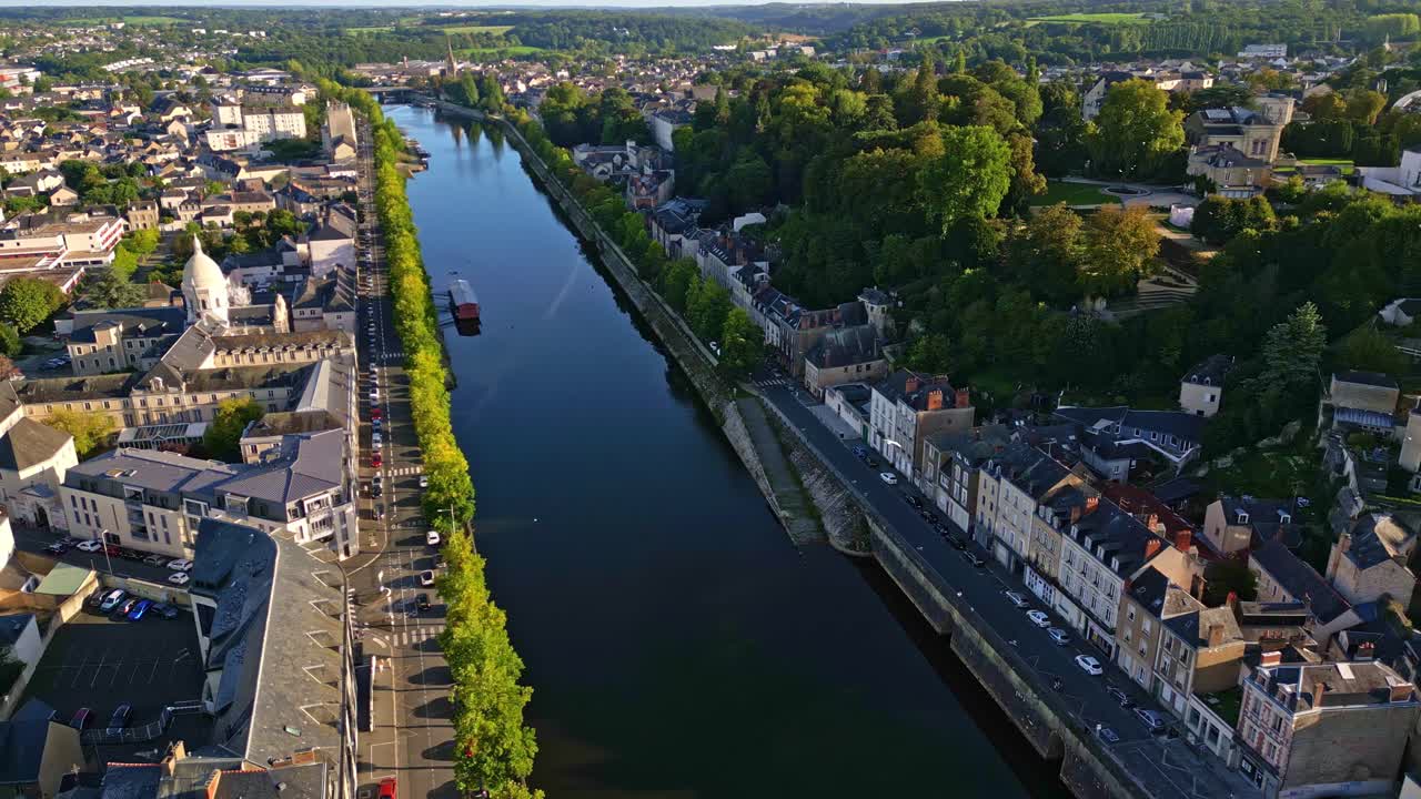 Immagine aerea del fiume Mayenne che scorre accanto allo storico Chateau Laval, immerso in una vegetazione lussureggiante e illuminato dalla luce dorata del sole