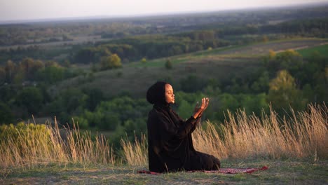 4k salah. african woman in black robe sitting on the carpet and pray in god. islamic religion