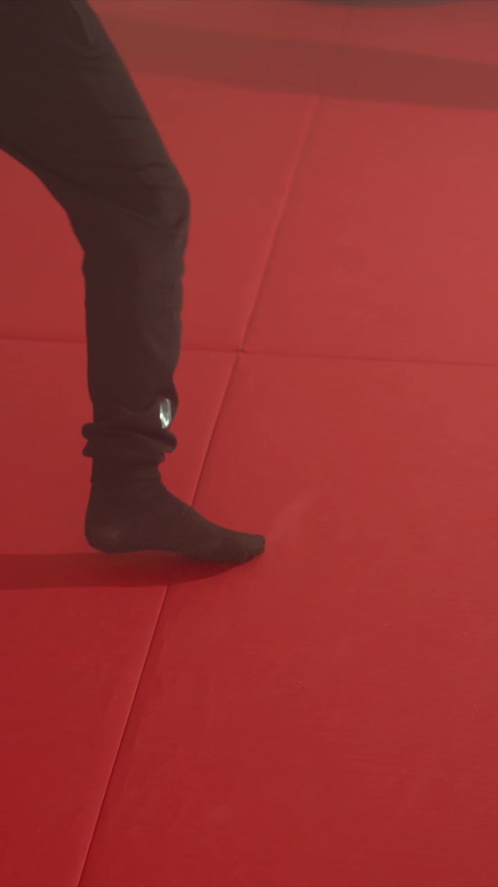 Close up of feet and legs performing footwork on red padded floor. Foot movements include stepping walking. Red flooring dominates scene with consistent texture
