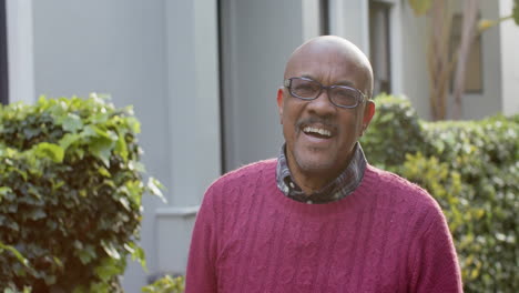 portrait of happy senior african american man in glasses laughing in sunny garden, slow motion