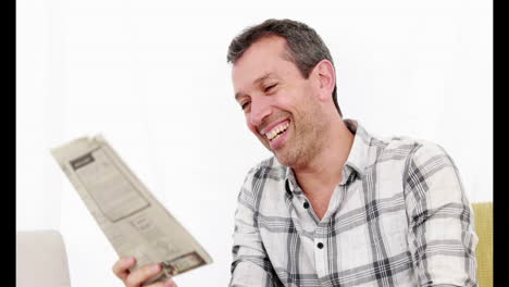 Smiling-man-reading-newspaper-while-sitting-on-the-couch