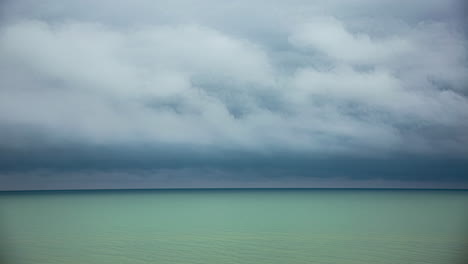 Storm-cloud-time-lapse-above-green-ocean-water,-space-for-text-on-horizon