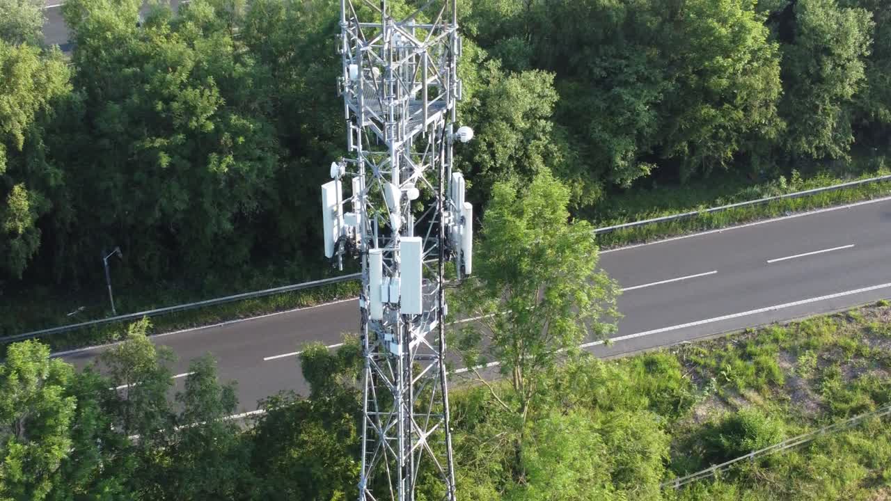 antena de torre de transmisión 5g en el campo británico con vehículos que viajan en la vista de órbita aérea de fondo de la carretera izquierda