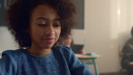 Cheerful-african-american-girl-sitting-at-desk-with-tablet-computer-in-school