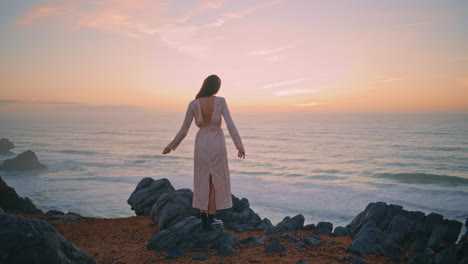 Slim lady standing rocks looking calm ocean alone back view. Girl raising hands