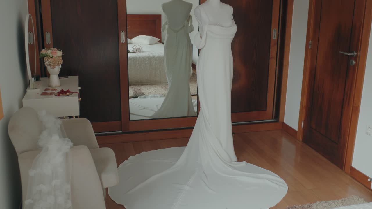 White wedding dress with long train displayed on mannequin in bedroom