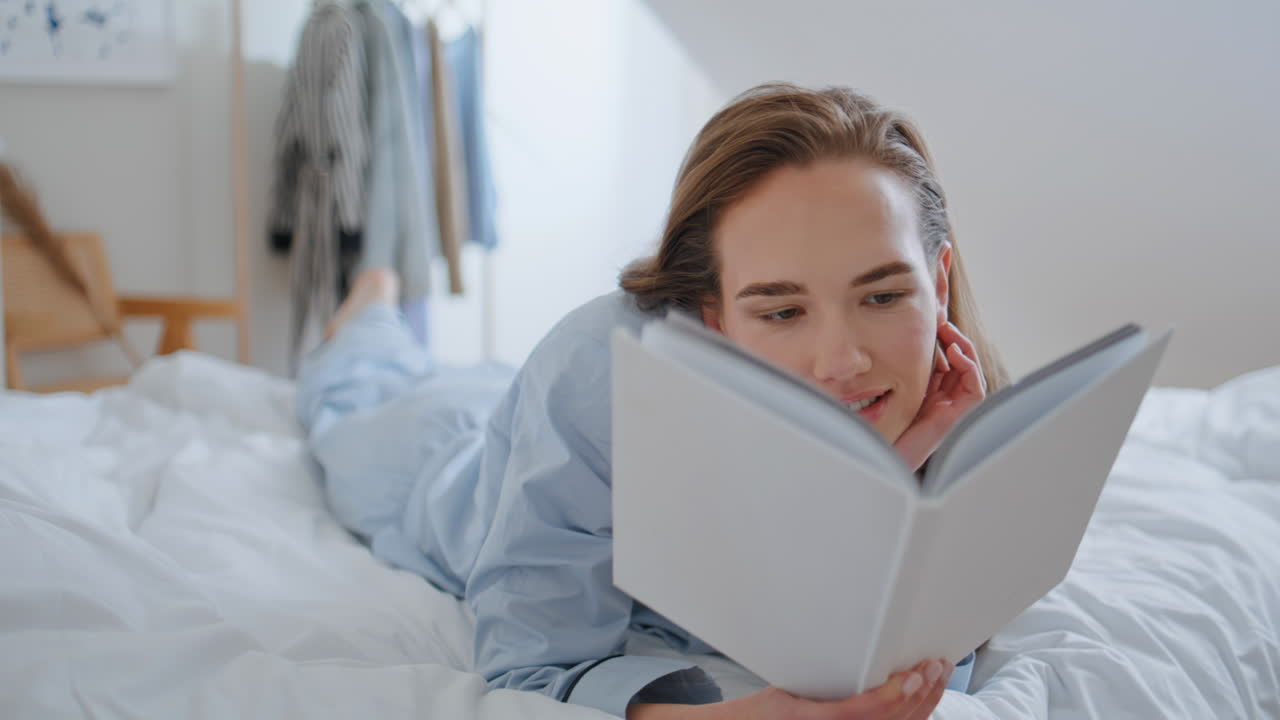 Nahaufnahme einer Frau, die ein Buch liest und gemütlich im Bett liegt. Studentin vertieft in einen Roman