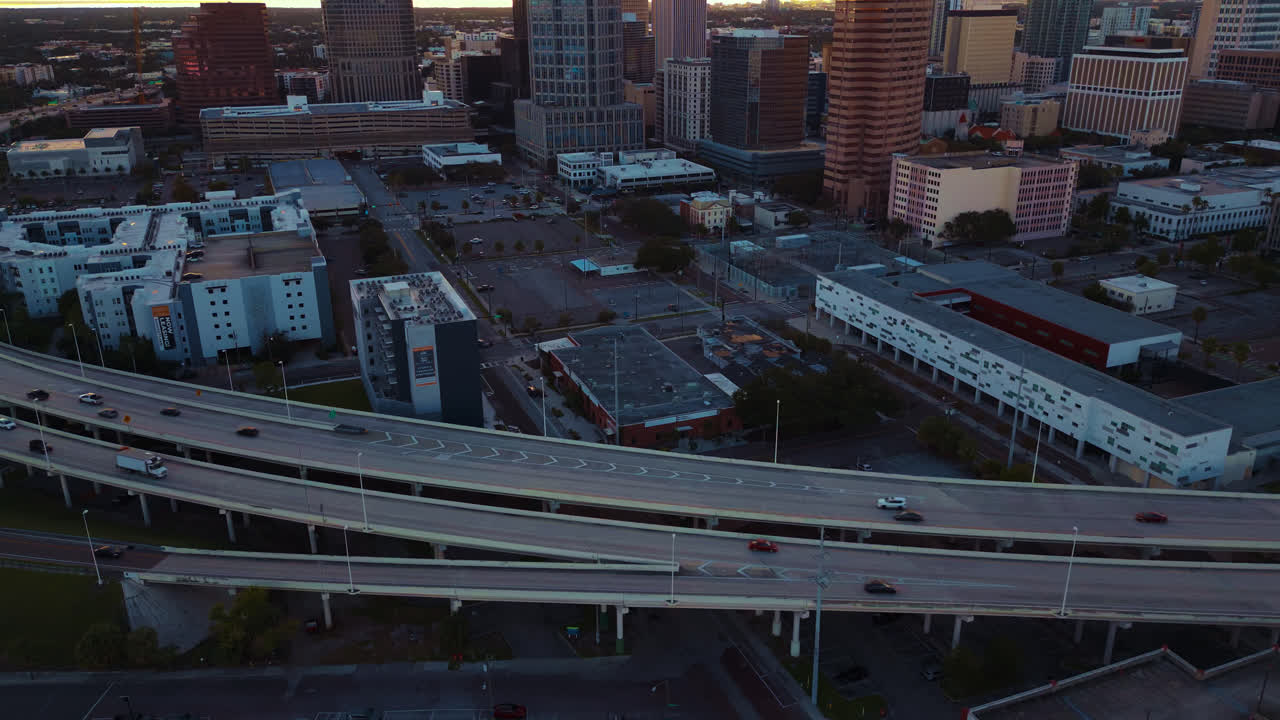Aerial view of a highway in Tampa as busy cars driving along as the day ends and sunset is beginning with skyscrapers in the background, Panning to the right