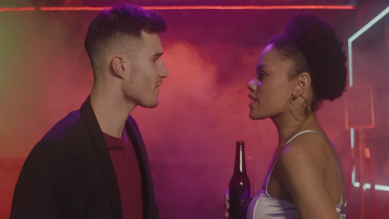 feliz pareja multiétnica bebiendo cerveza y bailando en la discoteca 1