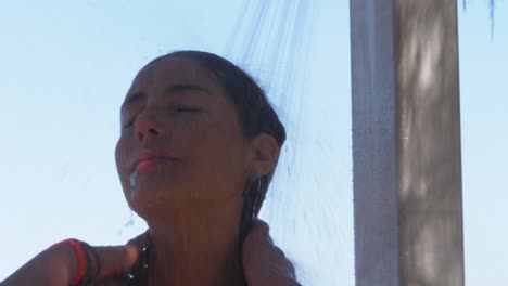 tanned woman washing face under the shower then smiled at the camera - taking a shower at duranbah beach after swimming - new south wales, australia