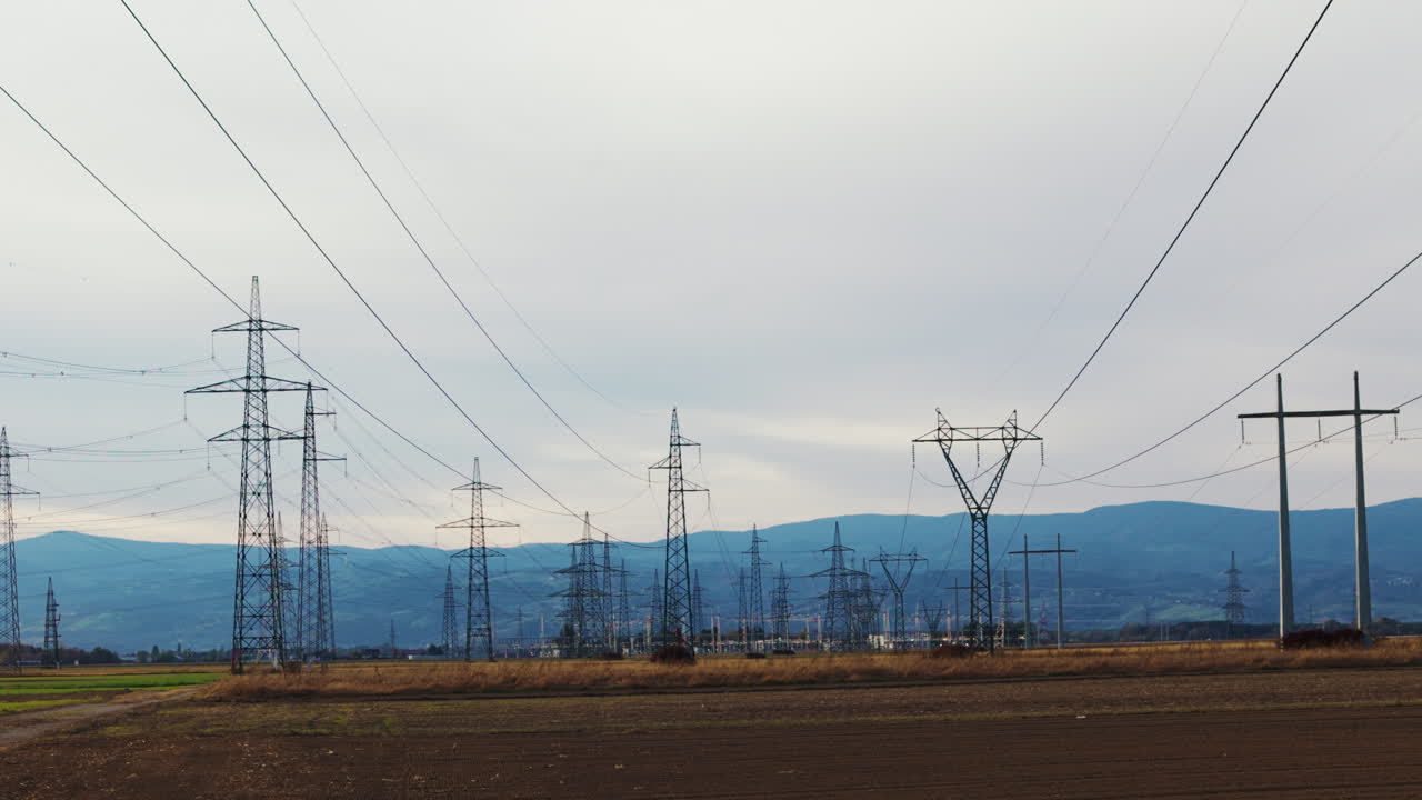 Electricity pylons and power lines stretch across fields and hills during sunset in a rural area